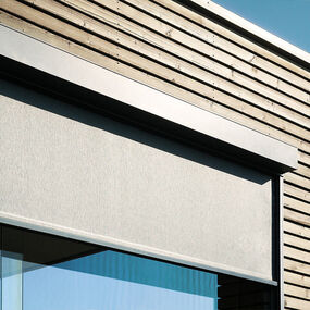 Moderner Sonnenschutz als Außenrollo an einem Fenster mit Holzfassade und Glasfront.