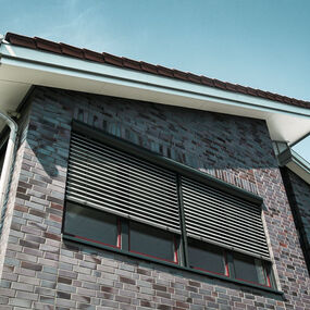 Modernes Wohnhaus mit Klinkerfassade und außenliegenden Jalousien am Fenster.